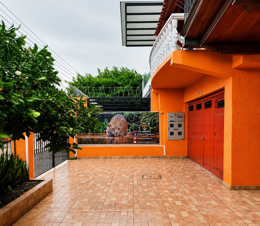 Exterior de El Jaguar Casa Hotel con muros naranja, patio con baldosas y gran letrero con jaguar